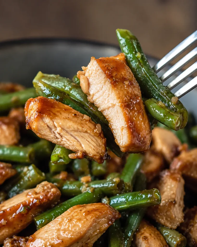 Close-up of chicken and green beans lifted with a fork from the stir fry bowl