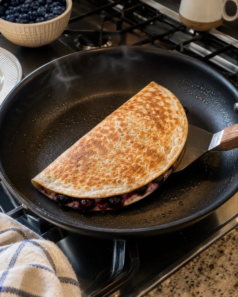 Blueberry breakfast quesadilla crisping in a skillet until golden brown