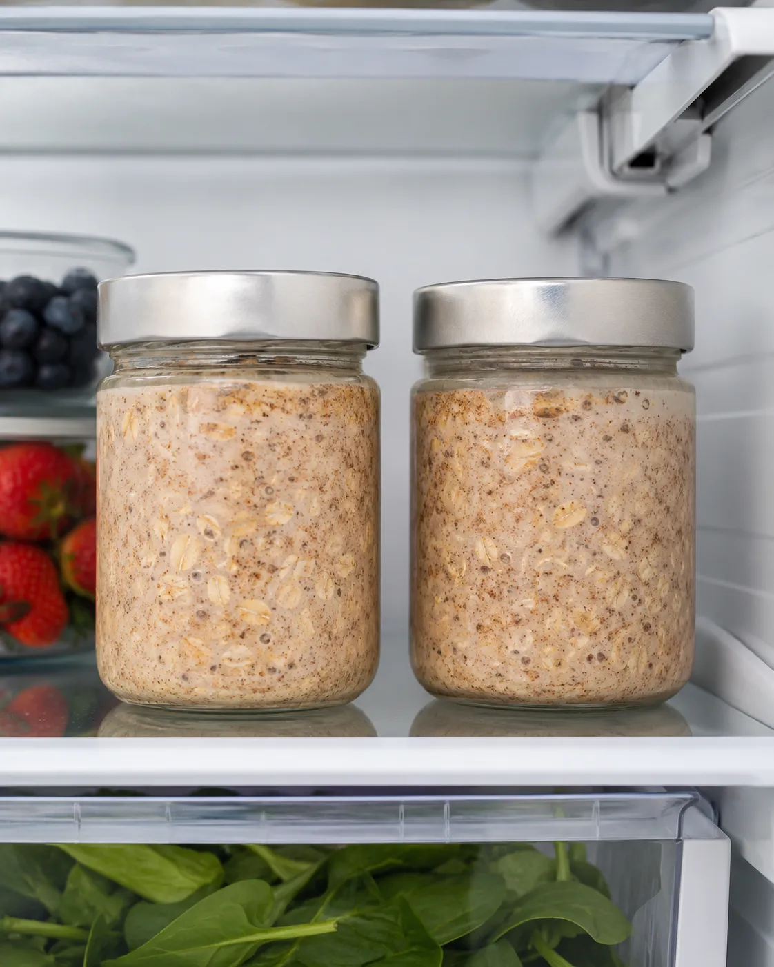 Two jars of creamy brown sugar overnight oats with cinnamon flecks stored in the refrigerator for meal prep