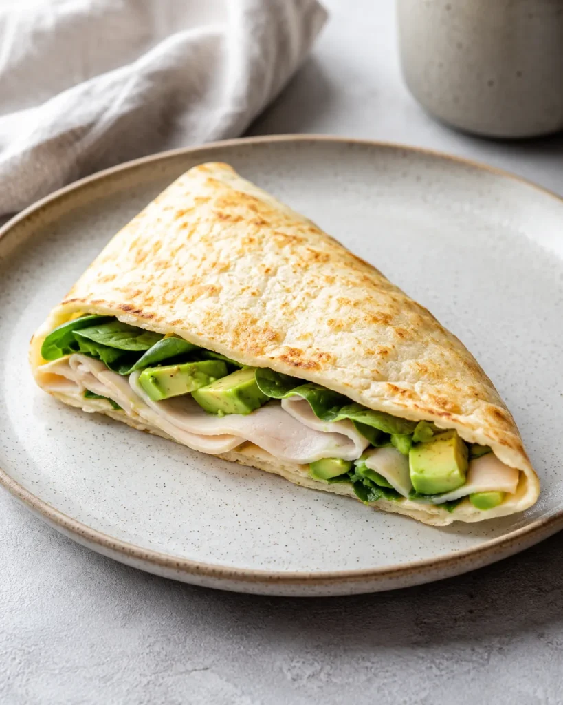 Folded cottage cheese flatbread wrap filled with turkey, greens, and avocado on a plate