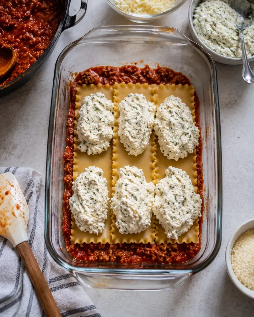 Lasagna being layered with sauce, noodles, and cottage cheese filling in a baking dish