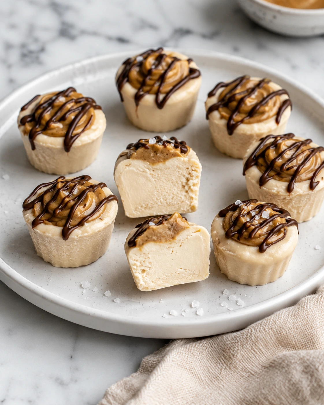 Frozen Greek yogurt peanut butter bites topped with peanut butter and chocolate drizzle on a white plate.