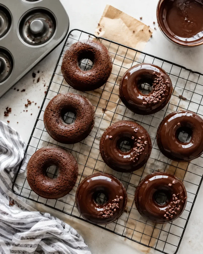 Baked high-protein chocolate donuts cooling on a rack beside a donut pan