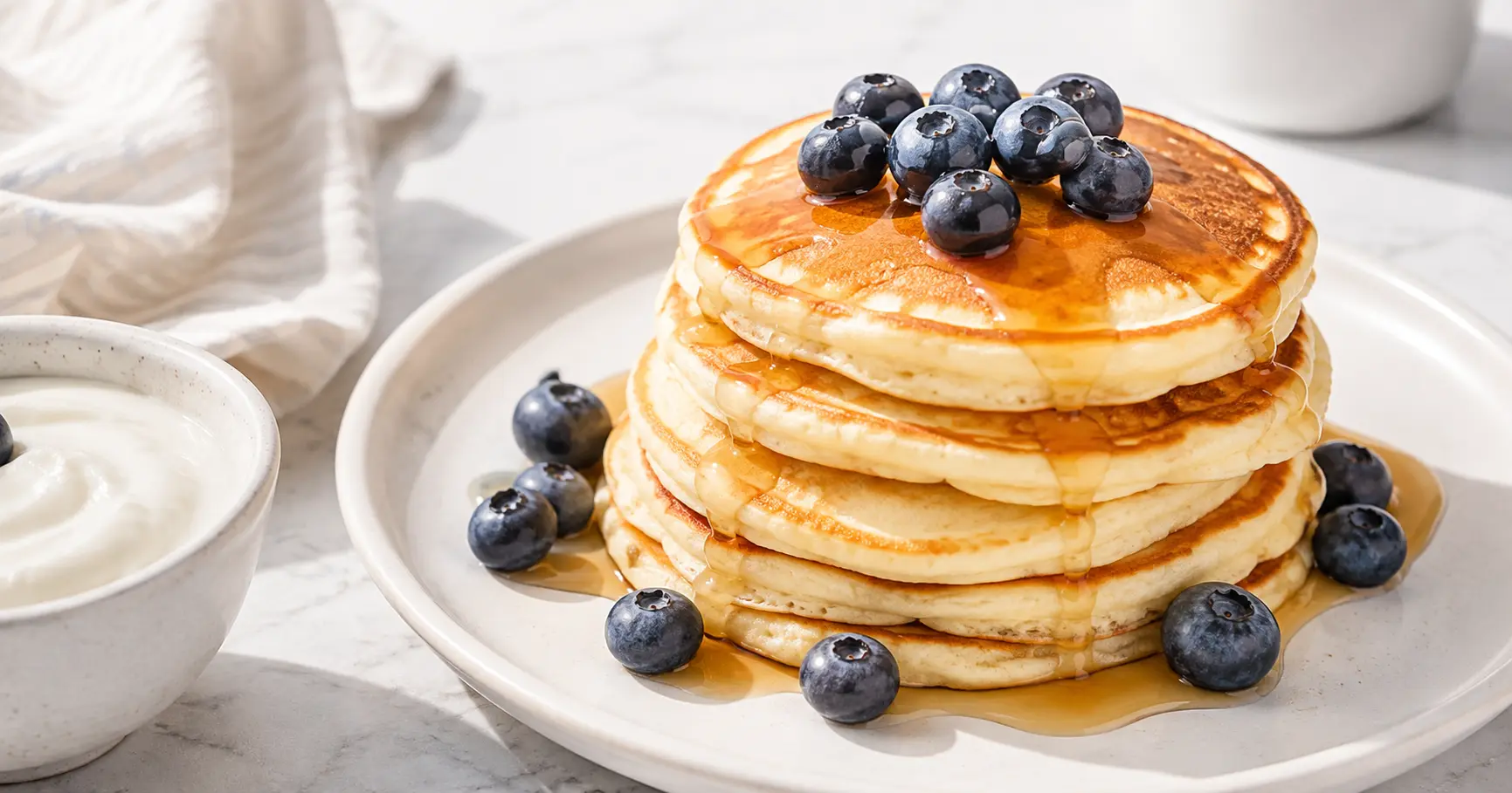 Protein Greek yogurt pancakes stacked on a plate with blueberries and maple syrup