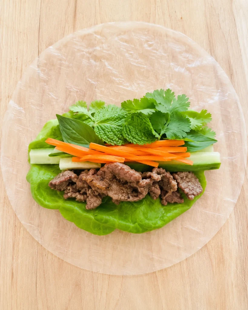 Thai basil beef rolls being assembled with rice paper, lettuce, herbs, and vegetables