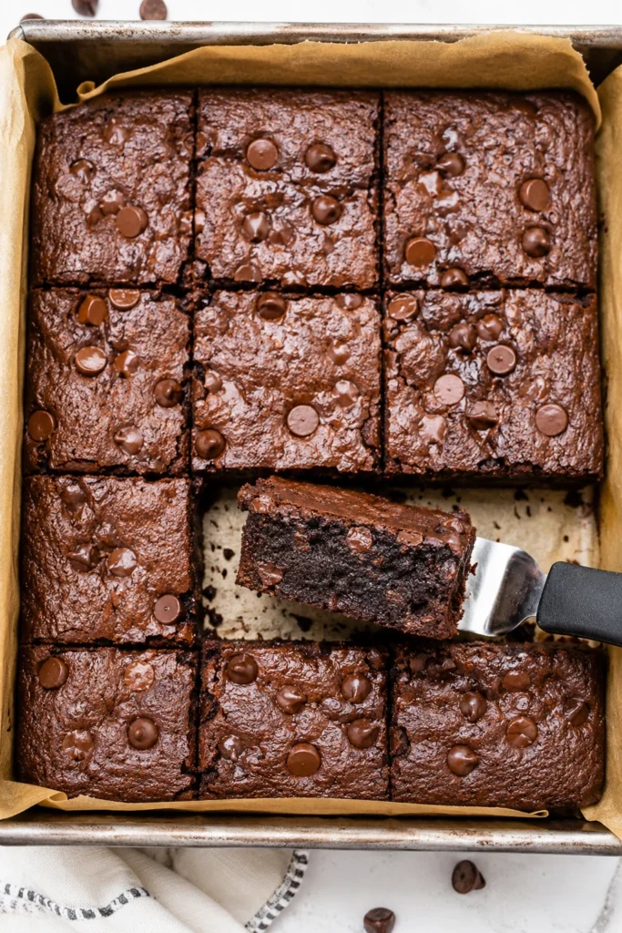Cut zero-sugar Greek yogurt brownies in a parchment-lined baking pan